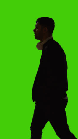 Vertical-Video-Silhouette-Of-Man-With-Wireless-Headphones-Walking-Across-Frame-Against-Green-Screen-1